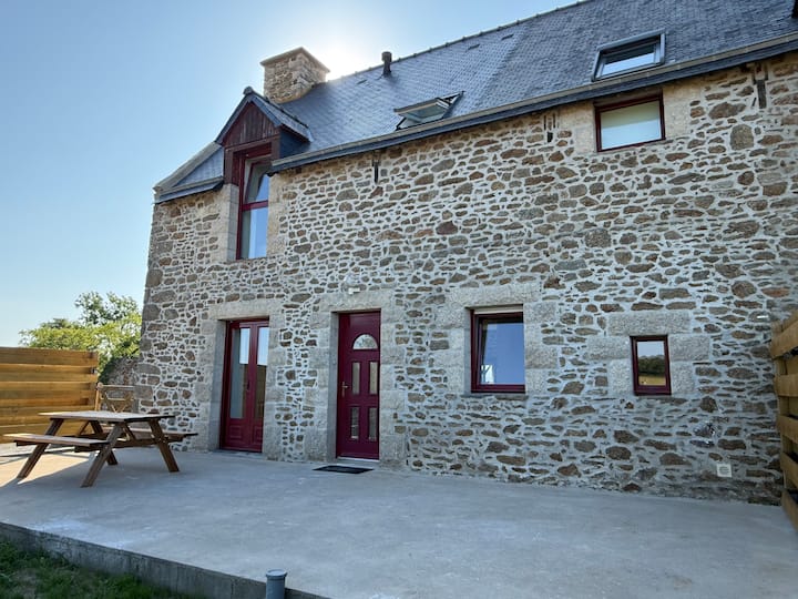 Façade en pierre du gîte Austral près de Saint-Malo avec portes rouges, terrasse béton et table pique-nique