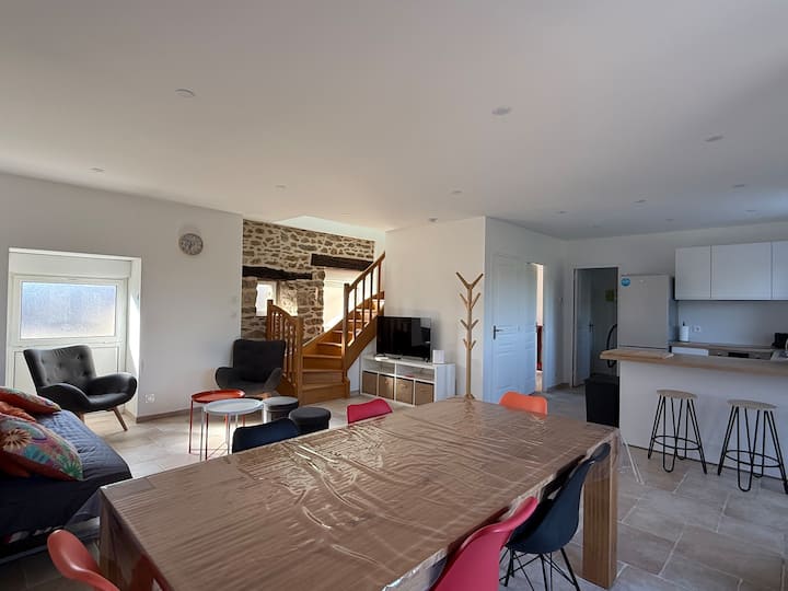 Salle à manger du gîte Austral avec mur en pierre bretonne apparente, table et escalier en bois