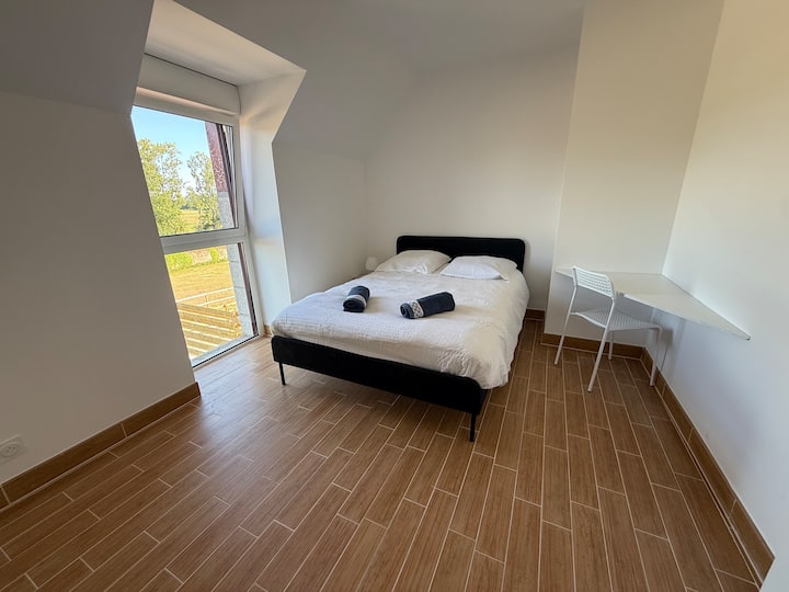 Chambre double avec lit noir et fenêtre donnant sur la campagne bretonne dans le gîte Austral près de Saint-Malo