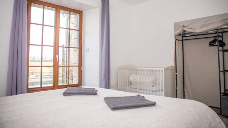 Chambre familiale avec lit double, lit bébé et fenêtre à petits carreaux donnant sur les pâtures du gîte Mistral