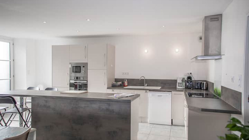 Cuisine entièrement équipée avec îlot central effet béton et hotte design dans le gîte Mistral à Saint-Malo